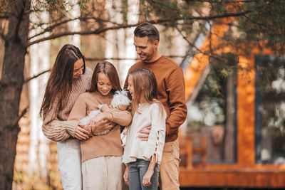 Cheerful family with dog standing outdoors