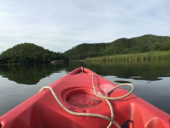 Red boat moored in lake against sky