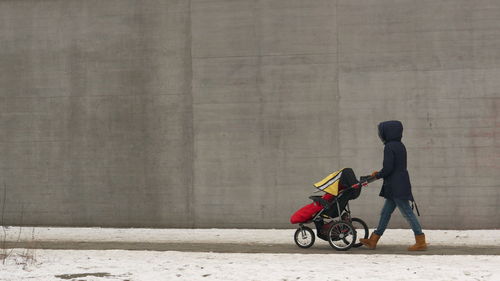 Side view of woman with baby carriage on road by wall