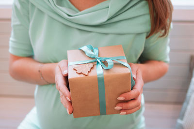 Pregnant woman in blue dress is holding gift box with christmas decorations. pregnant lifestyle.