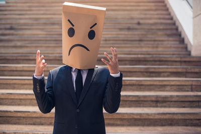 Businessman wearing angry paper mask on steps in city