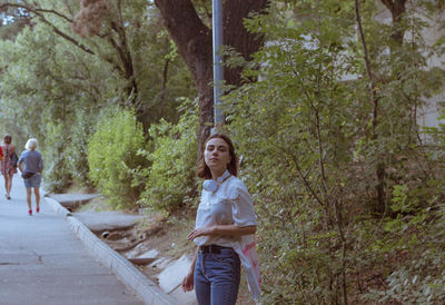 Woman standing on footpath amidst trees in forest