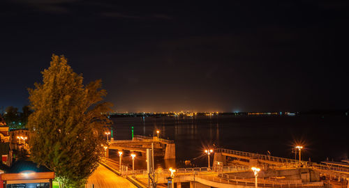 Illuminated buildings by river against sky at night