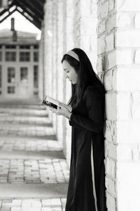 Portrait of young woman wearing ao dai standing against wall reading book