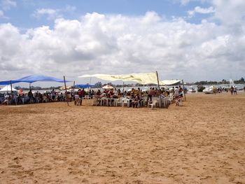 People on beach against cloudy sky