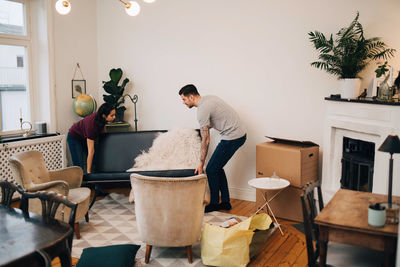 Man and woman arranging sofa in living room