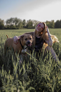 Young woman with dog sitting on grassy field against clear sky