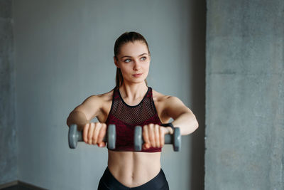 Young woman lifting dumbbells against wall