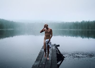 Full length of shirtless man standing on lake against sky