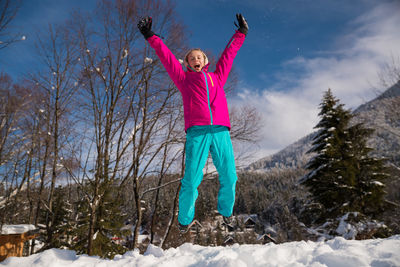 Full length of girl with arms raised jumping in snow during winter