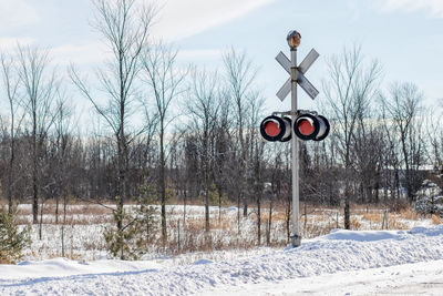 Railway signal by bare trees on snow covered field against sky
