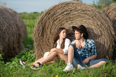 Young couple sitting on grass near the haystack 