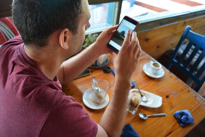 Rear view of man using mobile phone at table in cafe