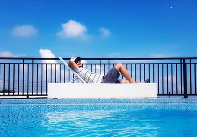 Woman sitting on swimming pool against sea