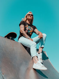 Blond woman sitting on a skating ramp with her skateboard