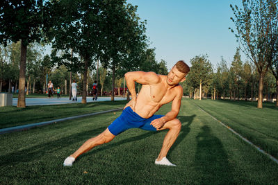 Full length of shirtless man with umbrella against trees