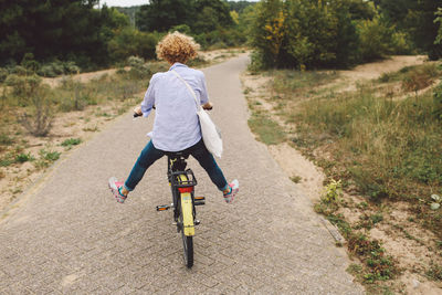 Rear view of carefree woman cycling on road