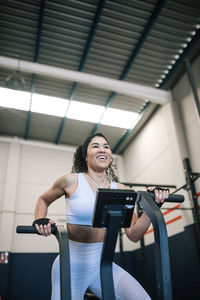 Happy sportswoman training on exercise bike in gym