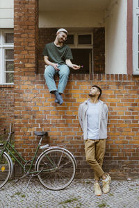 Smiling man giving flower to boyfriend standing by bicycle against brick wall