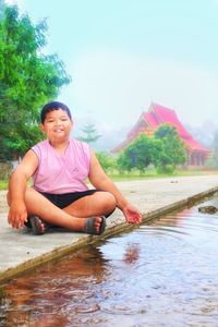 Portrait of man sitting by lake against sky