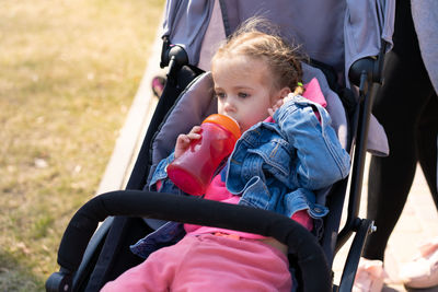 Girl drinking water from bottle while relaxing in stroller