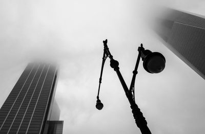 Low angle view of street light and buildings against cloudy sky