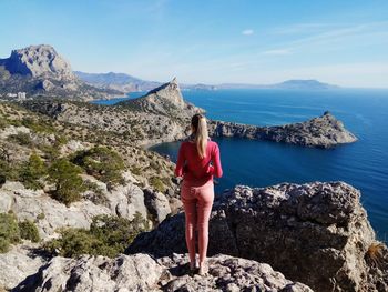 Rear view of woman standing on rock against sky
