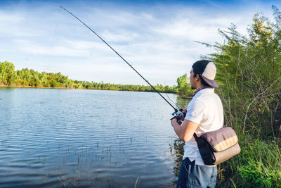 Man fishing in lake against sky