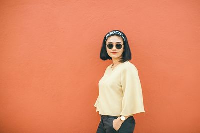 Portrait of young woman standing against wall