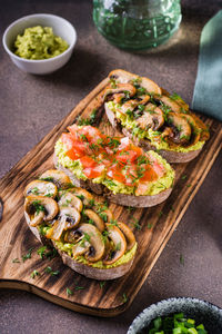 Sandwiches on rye bread with guacamole, fried mushrooms, tomatoes and dill on a board vertical view