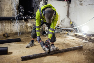 Plumber sawing pipe at illuminated basement