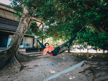 Happy asian teenager in casual outfit relaxing in hammock while using mobile phone. social media.