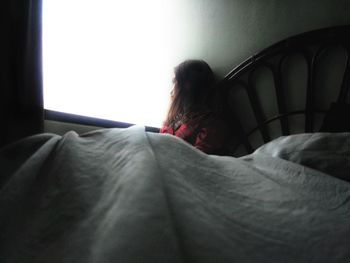 Rear view of woman sitting on bed at home