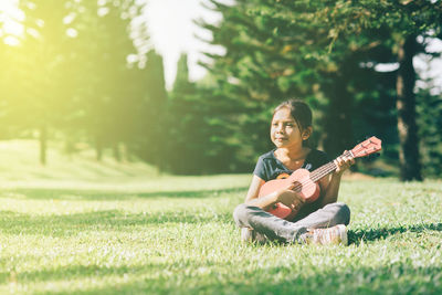 Girl playing guitar while sitting on grassy field at park