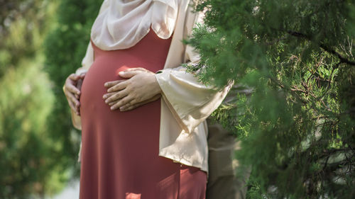 Rear view of man holding woman standing against trees