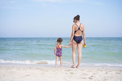 Rear view of father and daughter on beach against sky