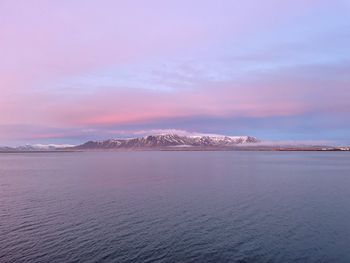 Scenic view of sea by snowcapped mountains against sky during sunset