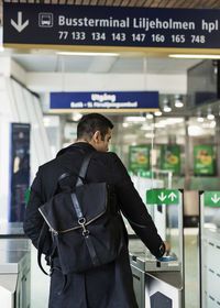 Rear view of man swiping ticket through turnstile at railroad station