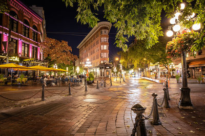 Illuminated street lights on sidewalk by buildings in city at night