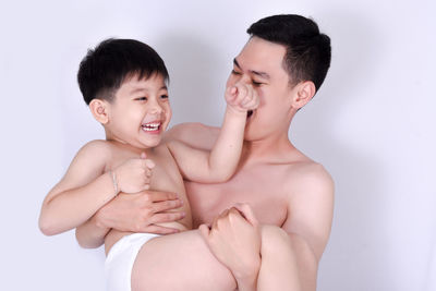 Shirtless father playing with son against white background