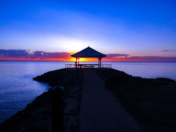 Silhouette lifeguard hut on beach against sky during sunset