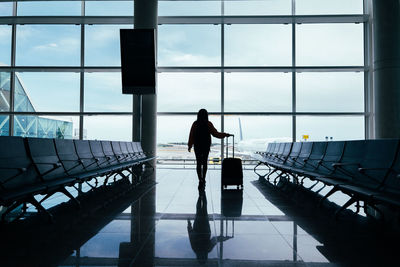 Woman with suitcase in hand, looks out the airport window while waiting for her flight.