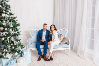 Portrait of couple sitting on sofa by christmas tree at home