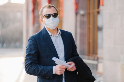 Portrait of businessman wearing mask and sunglasses while standing outdoors