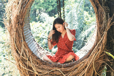 Thoughtful woman sitting on swing in forest