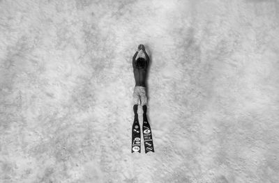 Directly above shot of shirtless man with diving flippers lying on shore at beach