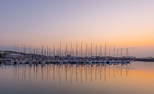 Reflection of sailboat moored in calm sea against clear sky during sunset