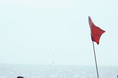 Red flag on sea against clear sky