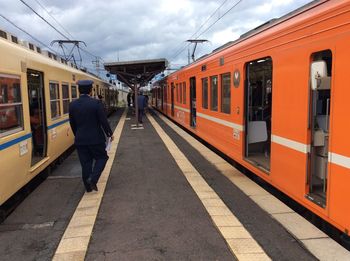 Rear view of train conductor on railroad station platform amidst trains against sky