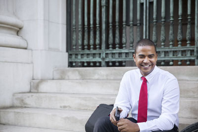 Happy businessman with mobile phone looking away while sitting on steps